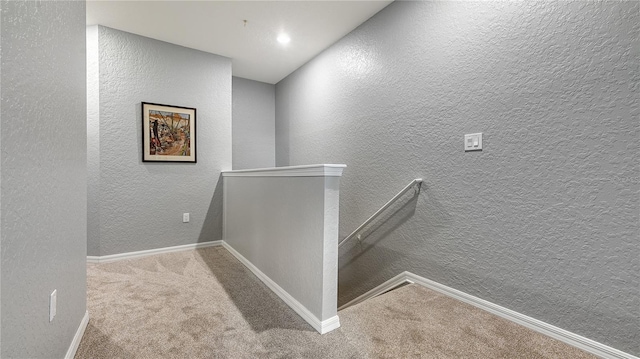 corridor featuring a textured wall, carpet, baseboards, and an upstairs landing