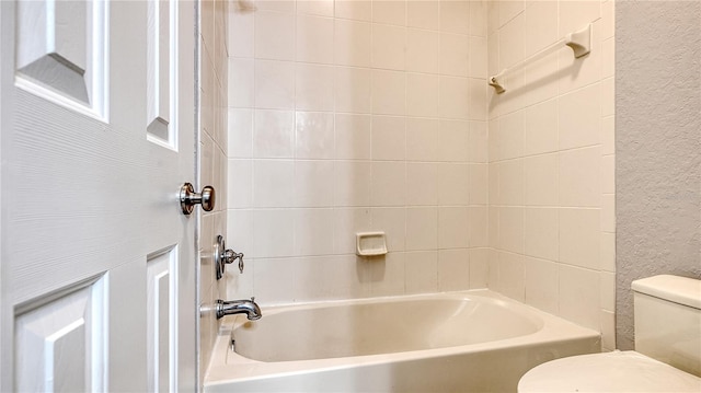 bathroom featuring a textured wall, tub / shower combination, and toilet