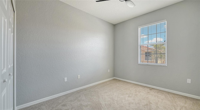 carpeted empty room featuring a textured wall, a ceiling fan, and baseboards