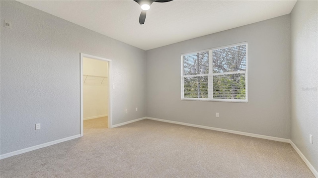 empty room featuring light carpet, a textured wall, and baseboards