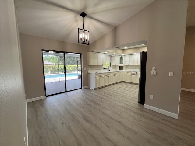 kitchen with pendant lighting, lofted ceiling, stainless steel refrigerator, white cabinets, and light wood-type flooring