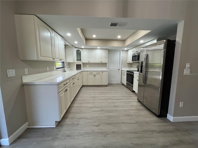 kitchen with sink, stainless steel appliances, light hardwood / wood-style floors, white cabinets, and a raised ceiling