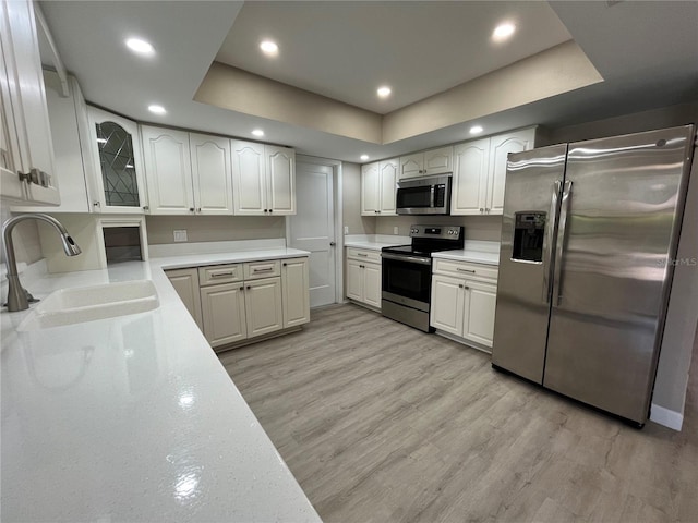 kitchen with sink, white cabinetry, light hardwood / wood-style flooring, appliances with stainless steel finishes, and a raised ceiling