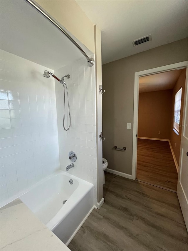 bathroom featuring hardwood / wood-style flooring, toilet, and tiled shower / bath combo