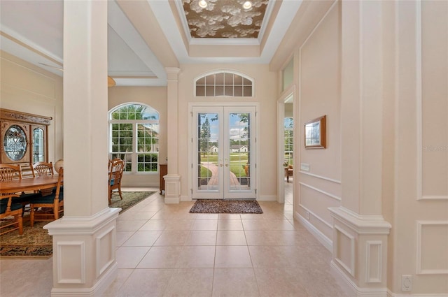 tiled entryway featuring french doors, ornate columns, crown molding, and a raised ceiling