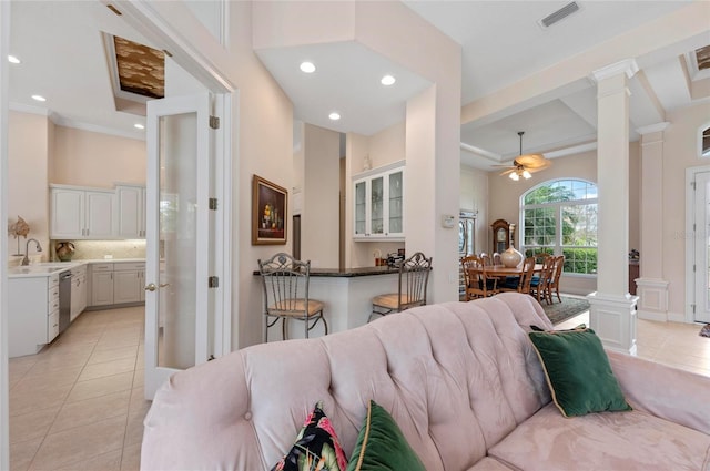 tiled living room with sink, decorative columns, ceiling fan, crown molding, and a high ceiling