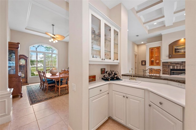 kitchen with coffered ceiling, light tile patterned floors, sink, white cabinets, and beam ceiling