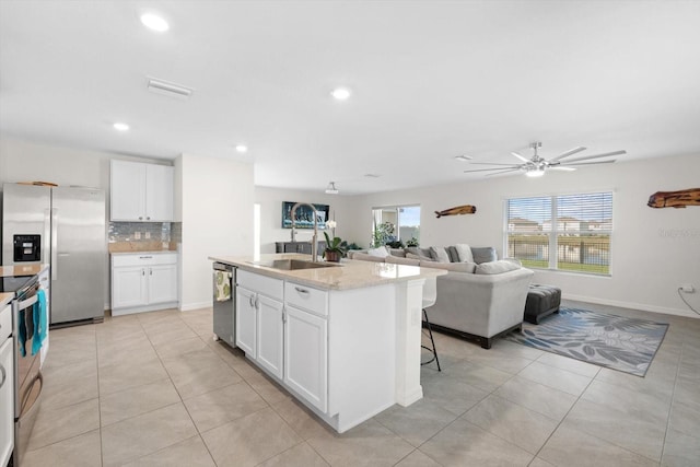 kitchen featuring light stone counters, stainless steel appliances, white cabinets, and a center island with sink