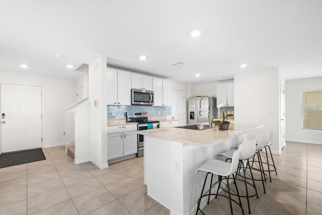 kitchen with white cabinetry, a kitchen breakfast bar, stainless steel appliances, tasteful backsplash, and an island with sink