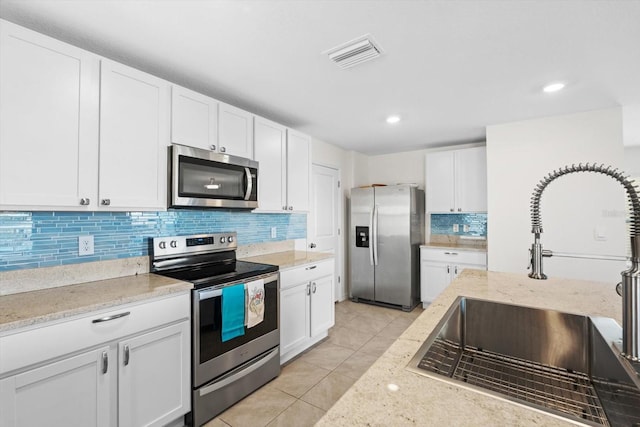 kitchen featuring sink, white cabinetry, light stone counters, stainless steel appliances, and backsplash