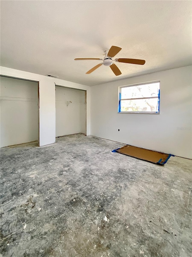 unfurnished bedroom with ceiling fan, two closets, and a textured ceiling