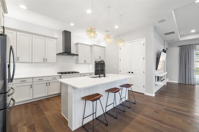 kitchen with decorative light fixtures, an island with sink, stainless steel appliances, dark wood-type flooring, and wall chimney exhaust hood