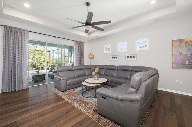 living room featuring a raised ceiling, dark wood-type flooring, and ceiling fan