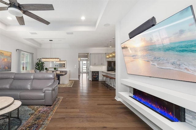 living room featuring ceiling fan, dark hardwood / wood-style floors, and a raised ceiling