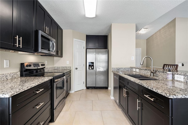 kitchen with sink, light tile patterned floors, stainless steel appliances, light stone counters, and a textured ceiling