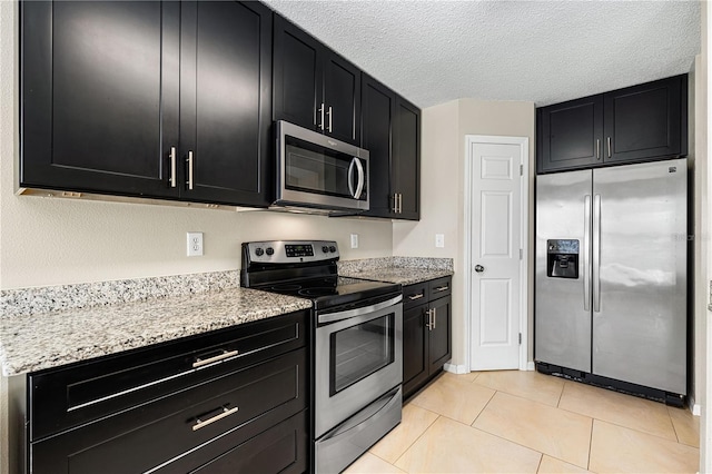 kitchen featuring light stone countertops, light tile patterned floors, stainless steel appliances, and a textured ceiling