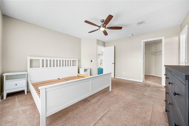 carpeted bedroom with ceiling fan, a walk in closet, a closet, and a textured ceiling