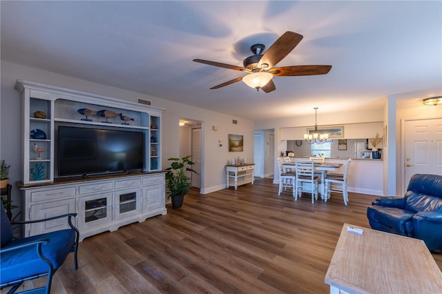 living room featuring dark wood finished floors, ceiling fan with notable chandelier, and baseboards