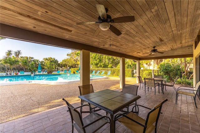 view of patio with a community pool, outdoor dining space, and a ceiling fan