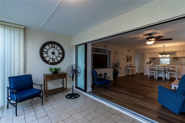 living area featuring ceiling fan with notable chandelier, light wood-type flooring, baseboards, and a textured wall