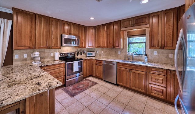 kitchen featuring light stone countertops, appliances with stainless steel finishes, brown cabinetry, and a sink