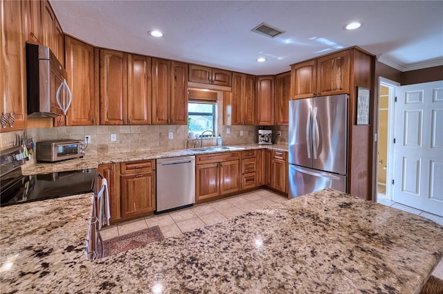 kitchen with appliances with stainless steel finishes, brown cabinets, a sink, and light stone counters