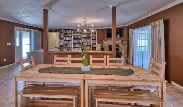 tiled dining space with an inviting chandelier, baseboards, ornamental molding, and a stone fireplace