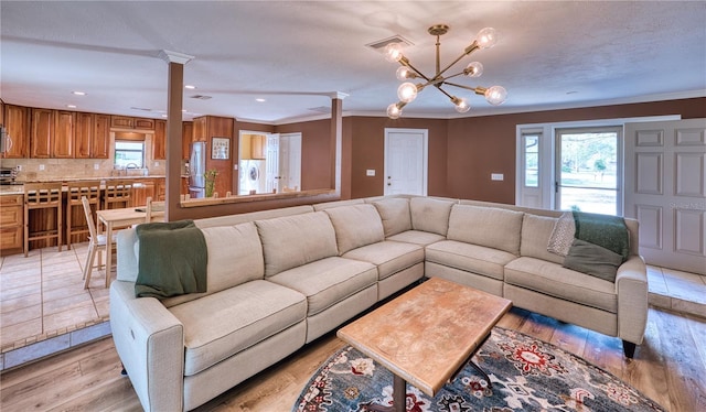 living area featuring crown molding, recessed lighting, decorative columns, and light wood-style flooring