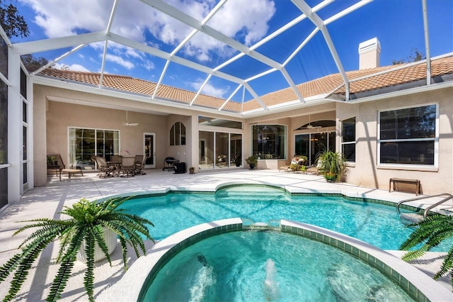 view of pool with glass enclosure, a pool with connected hot tub, ceiling fan, and a patio