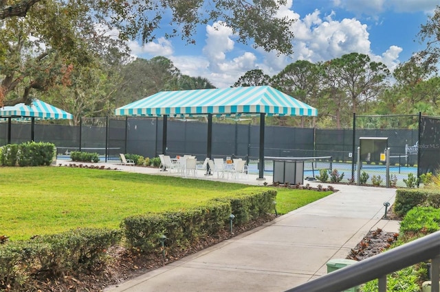 view of property's community featuring a tennis court, a lawn, and fence