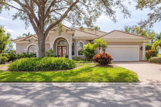 mediterranean / spanish home with a garage, a tiled roof, decorative driveway, and stucco siding