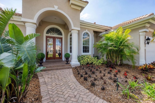 view of exterior entry featuring a garage, french doors, a tile roof, and stucco siding