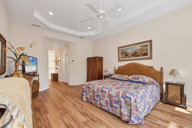 bedroom with a tray ceiling, visible vents, light wood-style flooring, and baseboards