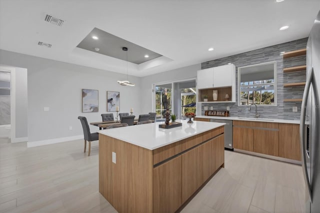 kitchen featuring pendant lighting, appliances with stainless steel finishes, white cabinets, a kitchen island, and a raised ceiling