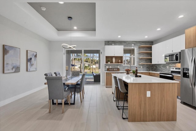 kitchen featuring decorative light fixtures, a raised ceiling, white cabinetry, a center island, and stainless steel appliances