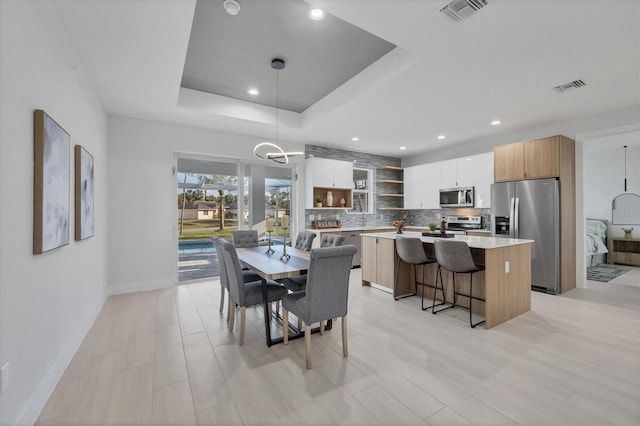 dining area featuring a raised ceiling and light hardwood / wood-style flooring