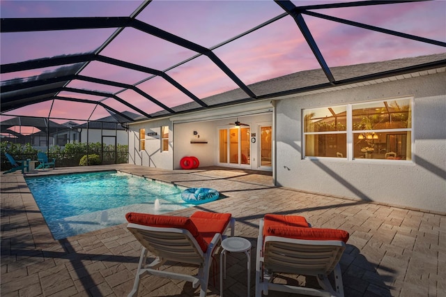 pool at dusk with ceiling fan, glass enclosure, a patio, and pool water feature