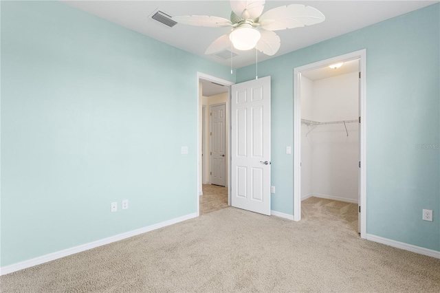 unfurnished bedroom with a spacious closet, light colored carpet, ceiling fan, and a closet