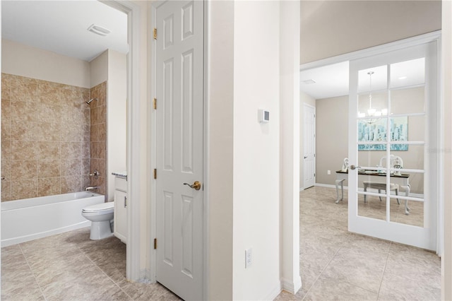 bathroom featuring tiled shower / bath, toilet, tile patterned floors, and an inviting chandelier