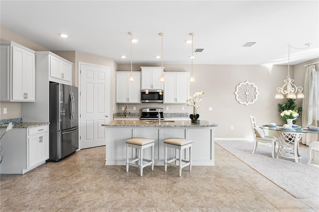 kitchen featuring appliances with stainless steel finishes, decorative light fixtures, white cabinetry, and a kitchen island with sink