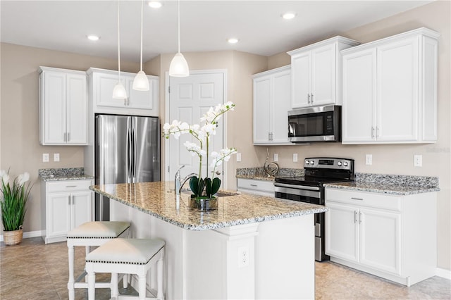 kitchen with a center island with sink, stainless steel appliances, hanging light fixtures, light stone countertops, and white cabinets