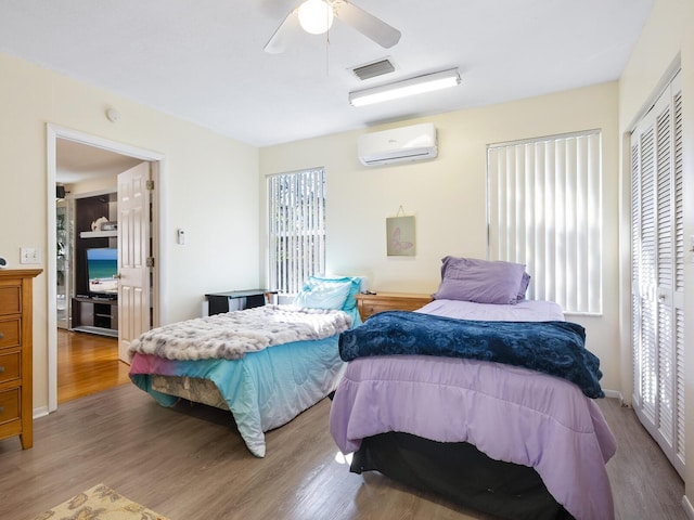 bedroom with ceiling fan, hardwood / wood-style floors, a wall unit AC, and a closet