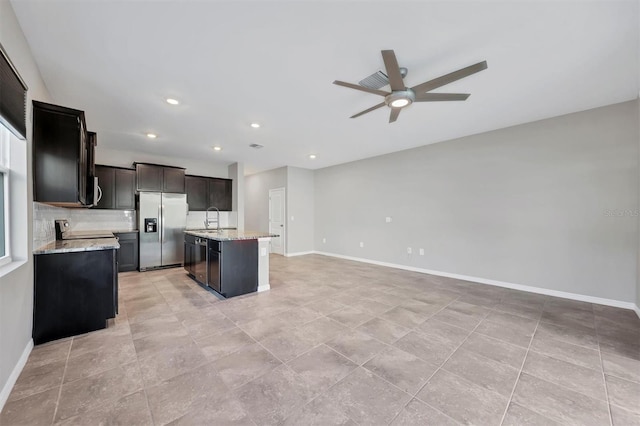 kitchen featuring sink, a center island with sink, light stone countertops, and stainless steel refrigerator with ice dispenser