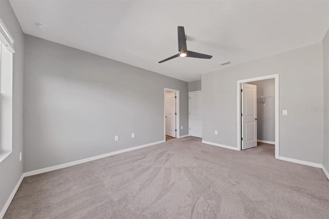 unfurnished bedroom featuring light carpet, a spacious closet, a closet, and ceiling fan