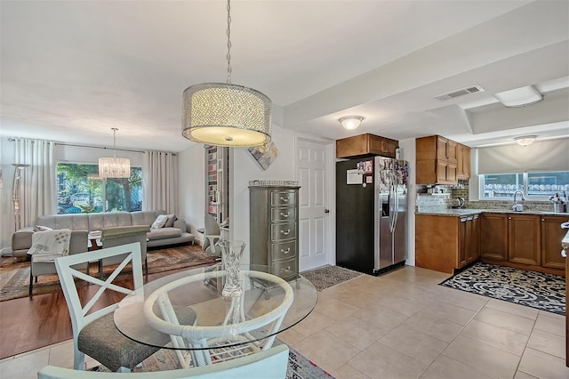 kitchen featuring light tile patterned flooring, pendant lighting, sink, stainless steel fridge with ice dispenser, and light stone countertops