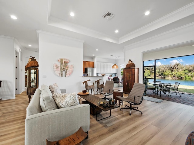 living room with crown molding, a raised ceiling, a water view, and light wood-type flooring