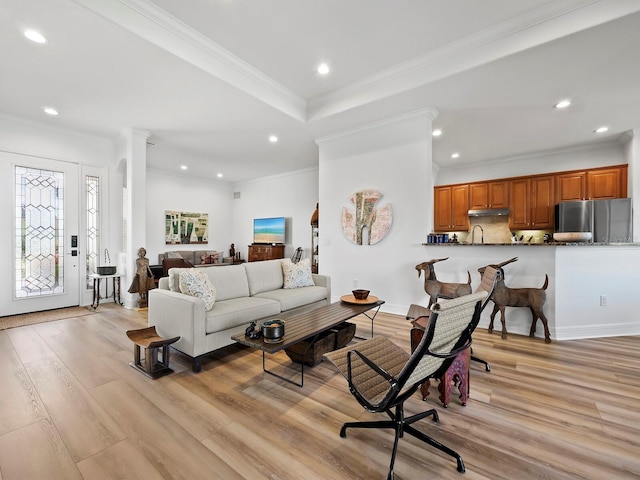 living room featuring sink, crown molding, light hardwood / wood-style floors, and ornate columns