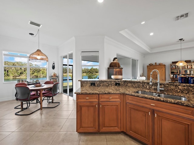 kitchen with ornamental molding, dark stone counters, decorative light fixtures, and sink