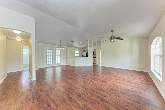 unfurnished living room featuring a wealth of natural light, lofted ceiling, dark hardwood / wood-style floors, and ceiling fan with notable chandelier