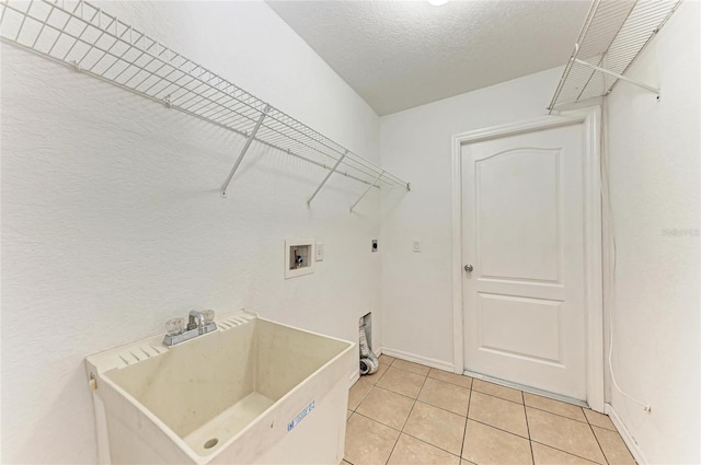 clothes washing area featuring sink, light tile patterned floors, hookup for a washing machine, electric dryer hookup, and a textured ceiling